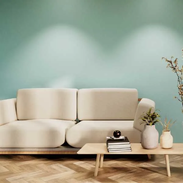 White couch in front of mint green wall, books and flower vases on a coffee table.